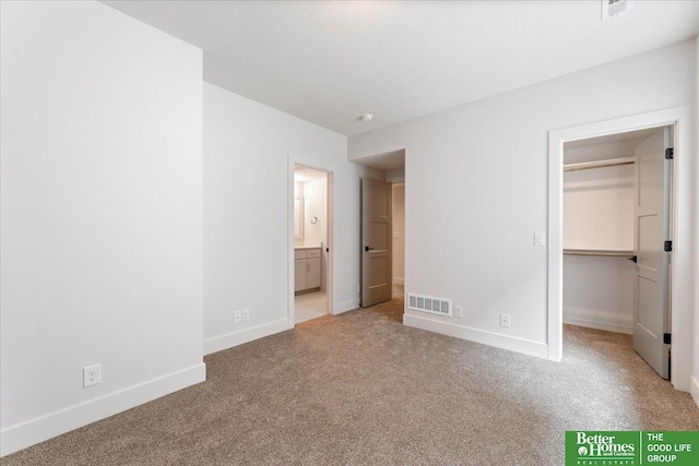 unfurnished bedroom featuring a closet, a walk in closet, light carpet, and ensuite bath