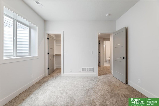 unfurnished bedroom with light colored carpet, a walk in closet, and a closet