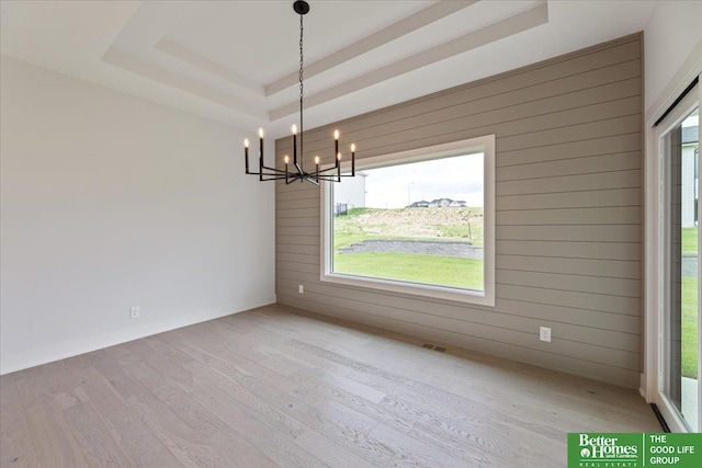 unfurnished dining area featuring a notable chandelier, light hardwood / wood-style floors, a raised ceiling, and wooden walls