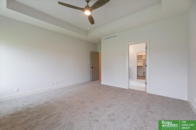 unfurnished bedroom with ceiling fan, a raised ceiling, a walk in closet, light carpet, and a closet