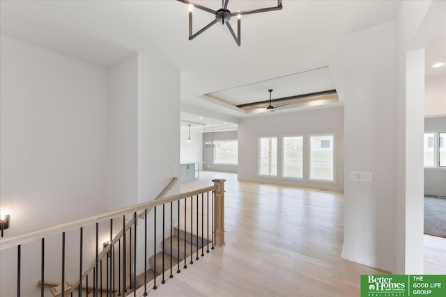 hallway featuring a raised ceiling, light wood-type flooring, and a notable chandelier