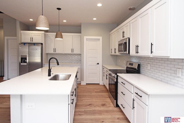 kitchen with sink, appliances with stainless steel finishes, pendant lighting, a kitchen island with sink, and white cabinets