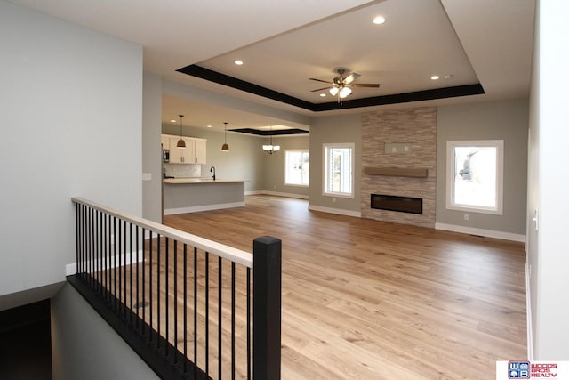 living room featuring a raised ceiling, ceiling fan with notable chandelier, a fireplace, and light hardwood / wood-style flooring