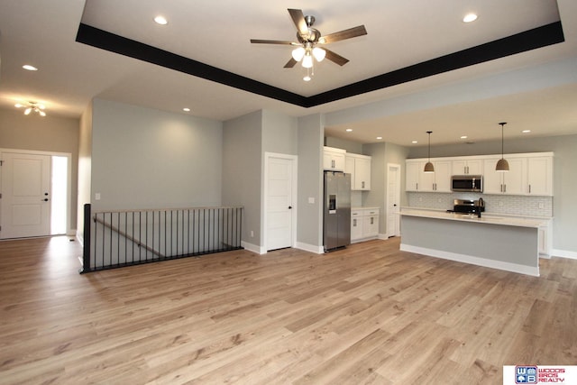 unfurnished living room with ceiling fan, a raised ceiling, and light hardwood / wood-style flooring