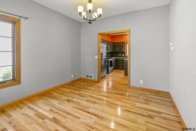 unfurnished room with a notable chandelier and light hardwood / wood-style floors