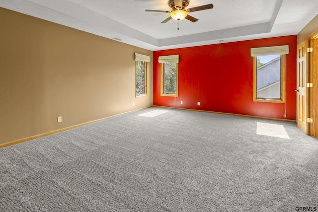 carpeted spare room with a raised ceiling and ceiling fan