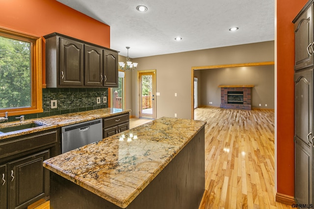 kitchen with a brick fireplace, stainless steel dishwasher, sink, a kitchen island, and hanging light fixtures