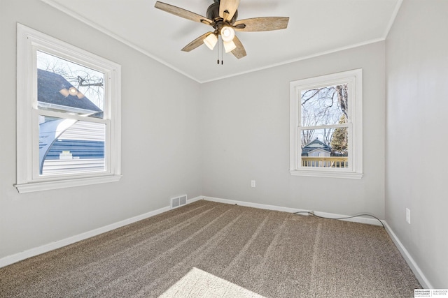 carpeted spare room with ceiling fan, ornamental molding, and a healthy amount of sunlight