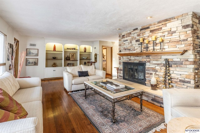 living room with a stone fireplace, dark hardwood / wood-style flooring, and a textured ceiling