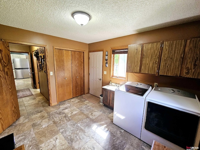 laundry area with washing machine and clothes dryer, sink, cabinets, and a textured ceiling