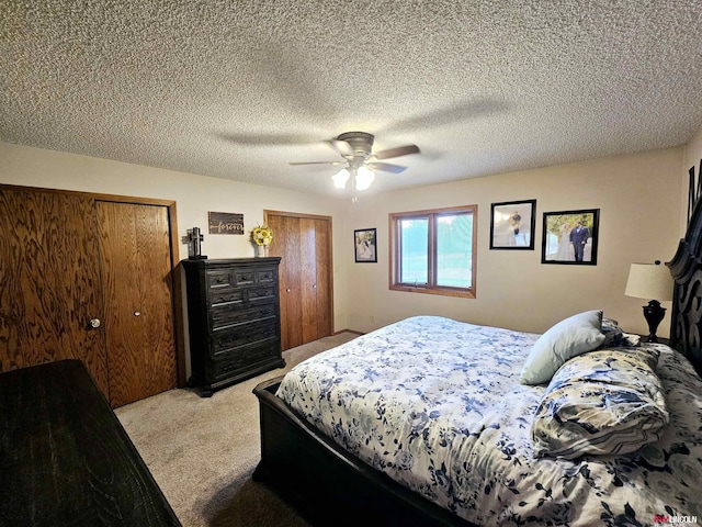 bedroom with a textured ceiling, ceiling fan, light carpet, and two closets