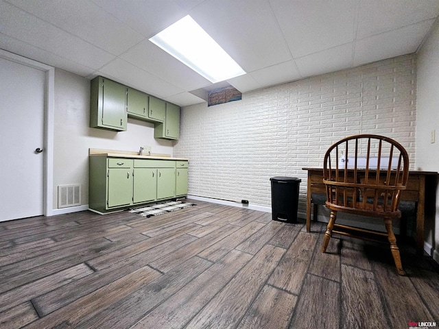 interior space featuring a drop ceiling, sink, brick wall, and green cabinetry