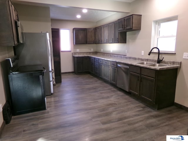 kitchen with appliances with stainless steel finishes, dark hardwood / wood-style flooring, dark brown cabinets, and sink