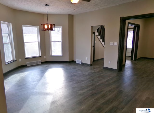 empty room with ceiling fan with notable chandelier, dark hardwood / wood-style floors, and a textured ceiling