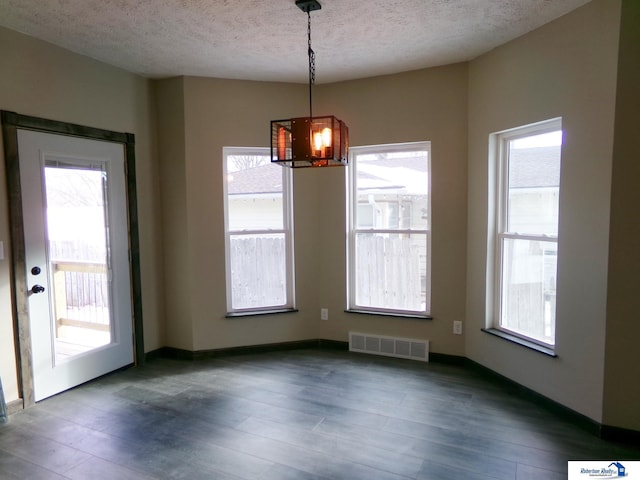 unfurnished dining area with dark hardwood / wood-style flooring, plenty of natural light, a chandelier, and a textured ceiling