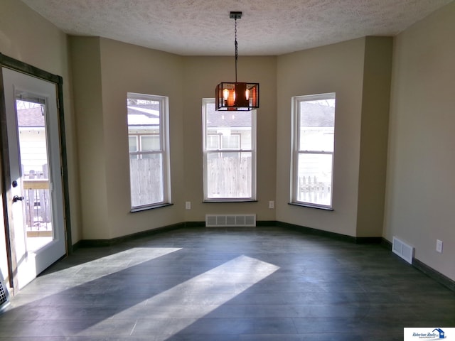 unfurnished dining area featuring a healthy amount of sunlight, a textured ceiling, and an inviting chandelier