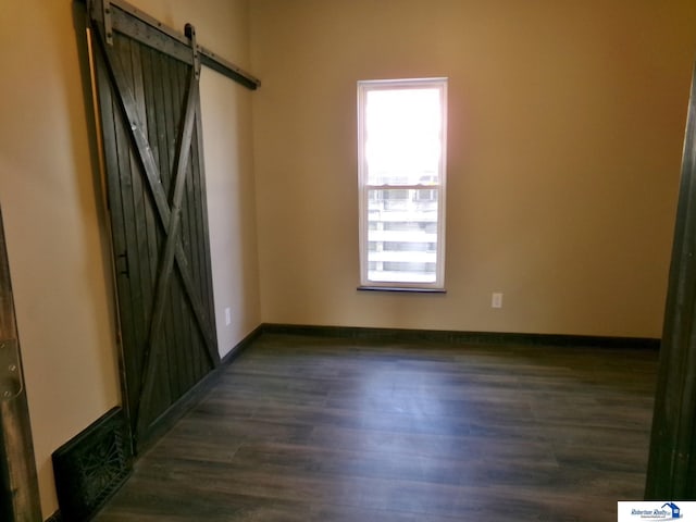 unfurnished room featuring a barn door and dark hardwood / wood-style floors