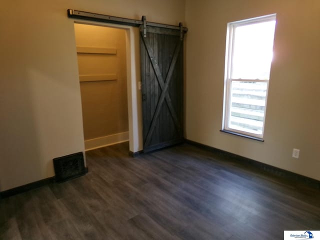 spare room with a barn door, dark wood-type flooring, and a healthy amount of sunlight