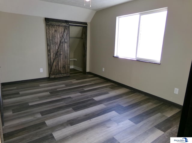 spare room with a barn door, vaulted ceiling, and dark wood-type flooring