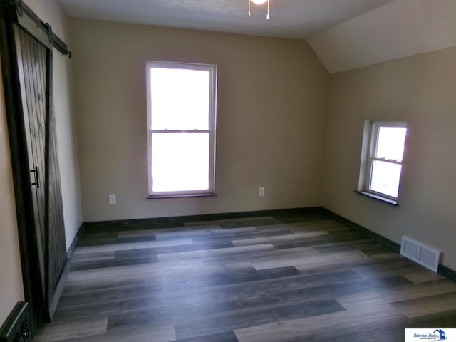 spare room featuring a barn door, plenty of natural light, dark hardwood / wood-style floors, and vaulted ceiling