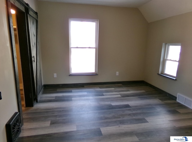 empty room featuring dark hardwood / wood-style floors, a barn door, a wealth of natural light, and vaulted ceiling