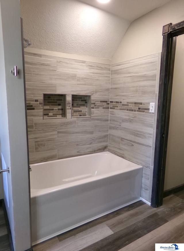 bathroom with vaulted ceiling, hardwood / wood-style floors, and tiled shower / bath combo