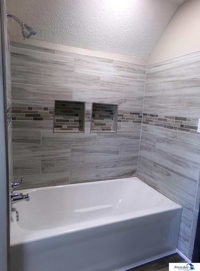 bathroom featuring a textured ceiling, tiled shower / bath combo, and lofted ceiling