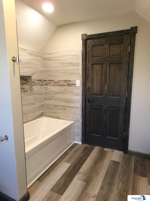 bathroom with vaulted ceiling, bathtub / shower combination, a textured ceiling, and hardwood / wood-style flooring