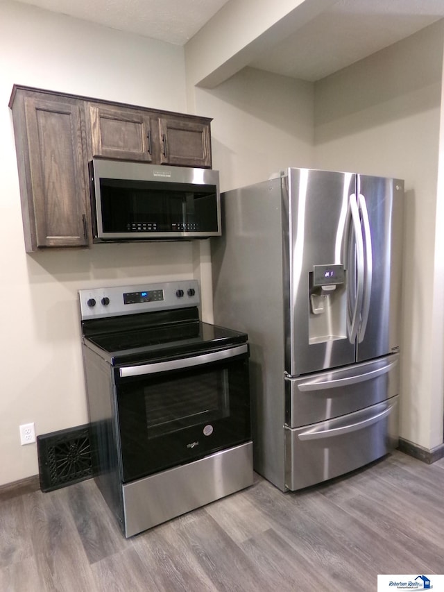 kitchen with dark brown cabinets, light hardwood / wood-style floors, and appliances with stainless steel finishes