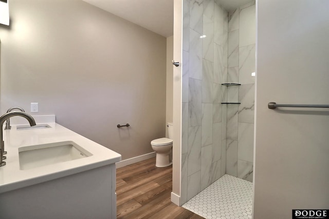 bathroom with hardwood / wood-style flooring, vanity, toilet, and a tile shower