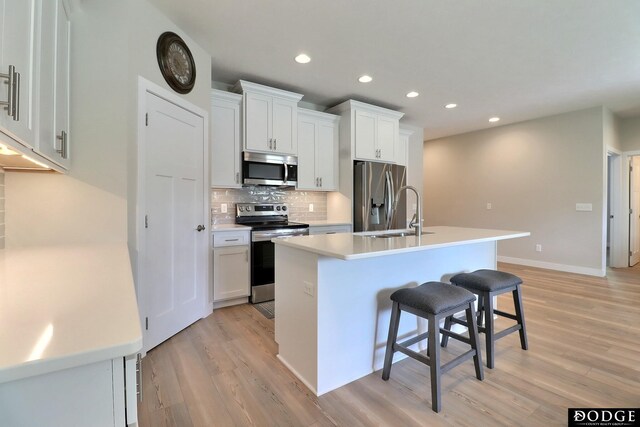 kitchen featuring light wood-type flooring, an island with sink, appliances with stainless steel finishes, white cabinetry, and a breakfast bar area