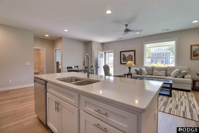 kitchen featuring stainless steel dishwasher, sink, light hardwood / wood-style floors, white cabinetry, and an island with sink