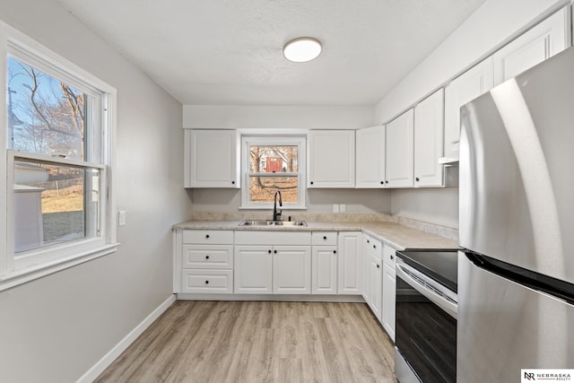 kitchen with sink, appliances with stainless steel finishes, a textured ceiling, white cabinets, and light wood-type flooring