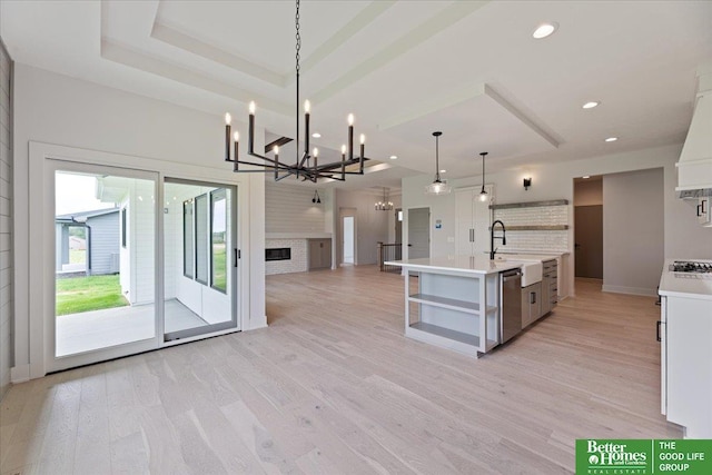 kitchen featuring a large island, dishwasher, pendant lighting, light hardwood / wood-style flooring, and an inviting chandelier