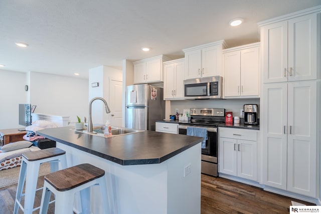 kitchen featuring dark wood-type flooring, stainless steel appliances, a center island with sink, white cabinetry, and sink