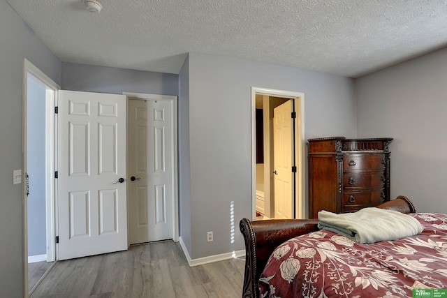 bedroom featuring ensuite bath, a textured ceiling, and light wood-type flooring