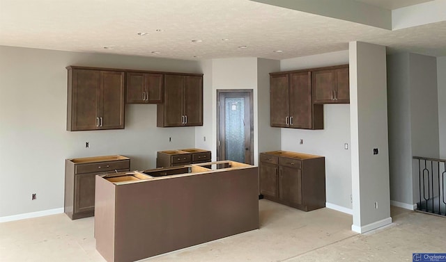 kitchen with dark brown cabinetry, a textured ceiling, a center island, and baseboards