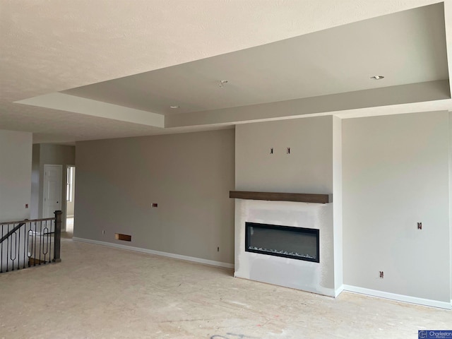 unfurnished living room with a glass covered fireplace, a raised ceiling, and baseboards