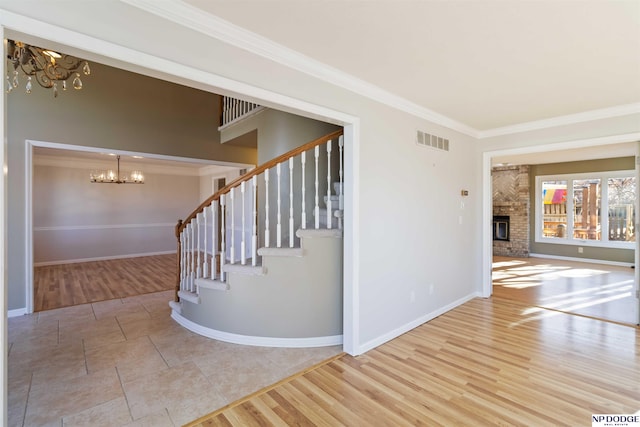 staircase featuring hardwood / wood-style floors, a fireplace, an inviting chandelier, and crown molding