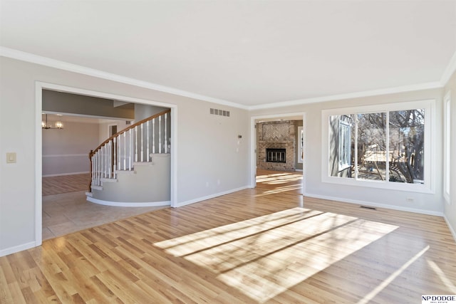 unfurnished living room with a brick fireplace, an inviting chandelier, light wood-type flooring, and ornamental molding