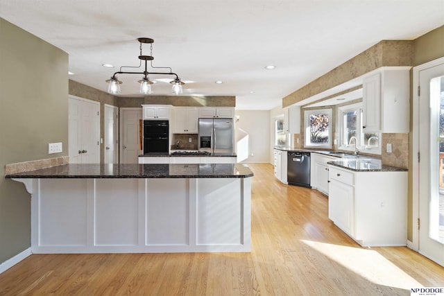 kitchen featuring decorative light fixtures, white cabinets, light wood-type flooring, dark stone countertops, and black appliances