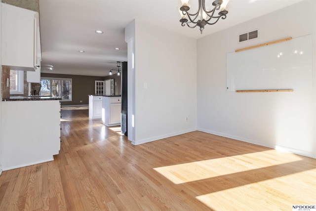 unfurnished dining area with light wood-type flooring and a notable chandelier