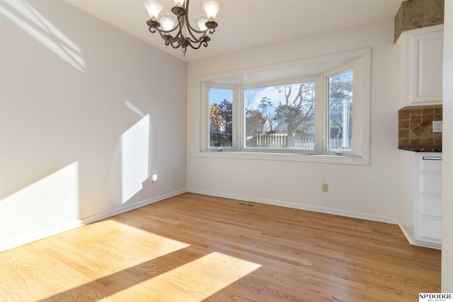 unfurnished dining area featuring an inviting chandelier and light hardwood / wood-style flooring