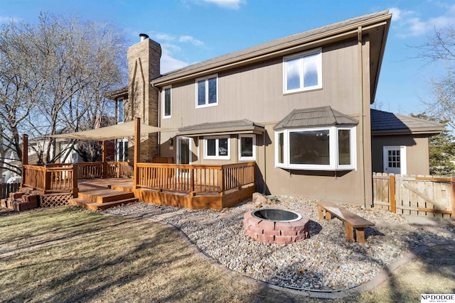 back of property with a yard, a wooden deck, and an outdoor fire pit