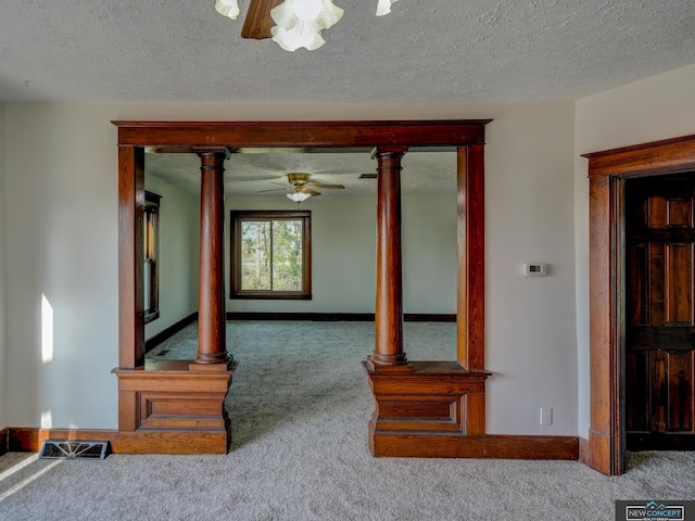 interior space with a textured ceiling, ceiling fan, ornate columns, and carpet