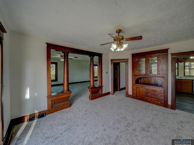 unfurnished bedroom with connected bathroom, dark colored carpet, ornate columns, ceiling fan, and a textured ceiling