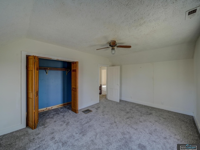 unfurnished bedroom with a textured ceiling, vaulted ceiling, a closet, carpet flooring, and ceiling fan