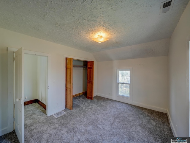 unfurnished bedroom featuring a textured ceiling, vaulted ceiling, multiple closets, and carpet flooring