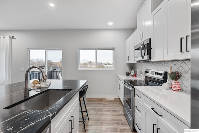 kitchen featuring appliances with stainless steel finishes, sink, white cabinets, light hardwood / wood-style flooring, and tasteful backsplash