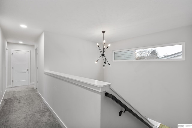 hallway featuring a notable chandelier and light carpet